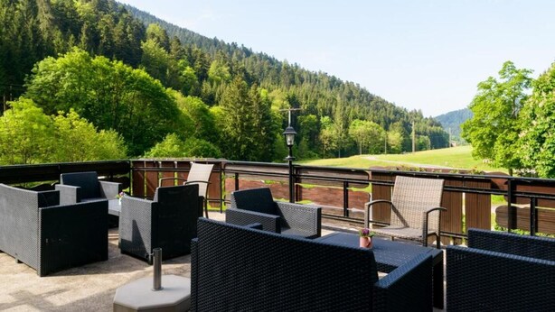 Ein Sitzbereich im Freien mit Korbmöbeln, einer Lampe und Blick auf ein bewaldetes Tal.