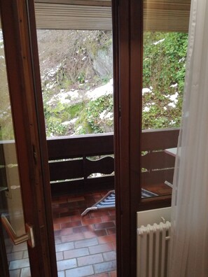 An open door leading to a balcony with a view of a garden and a brick floor.