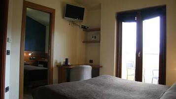 A hotel room with a bed, a desk with a chair, a television mounted on the wall, and a door leading to a balcony.