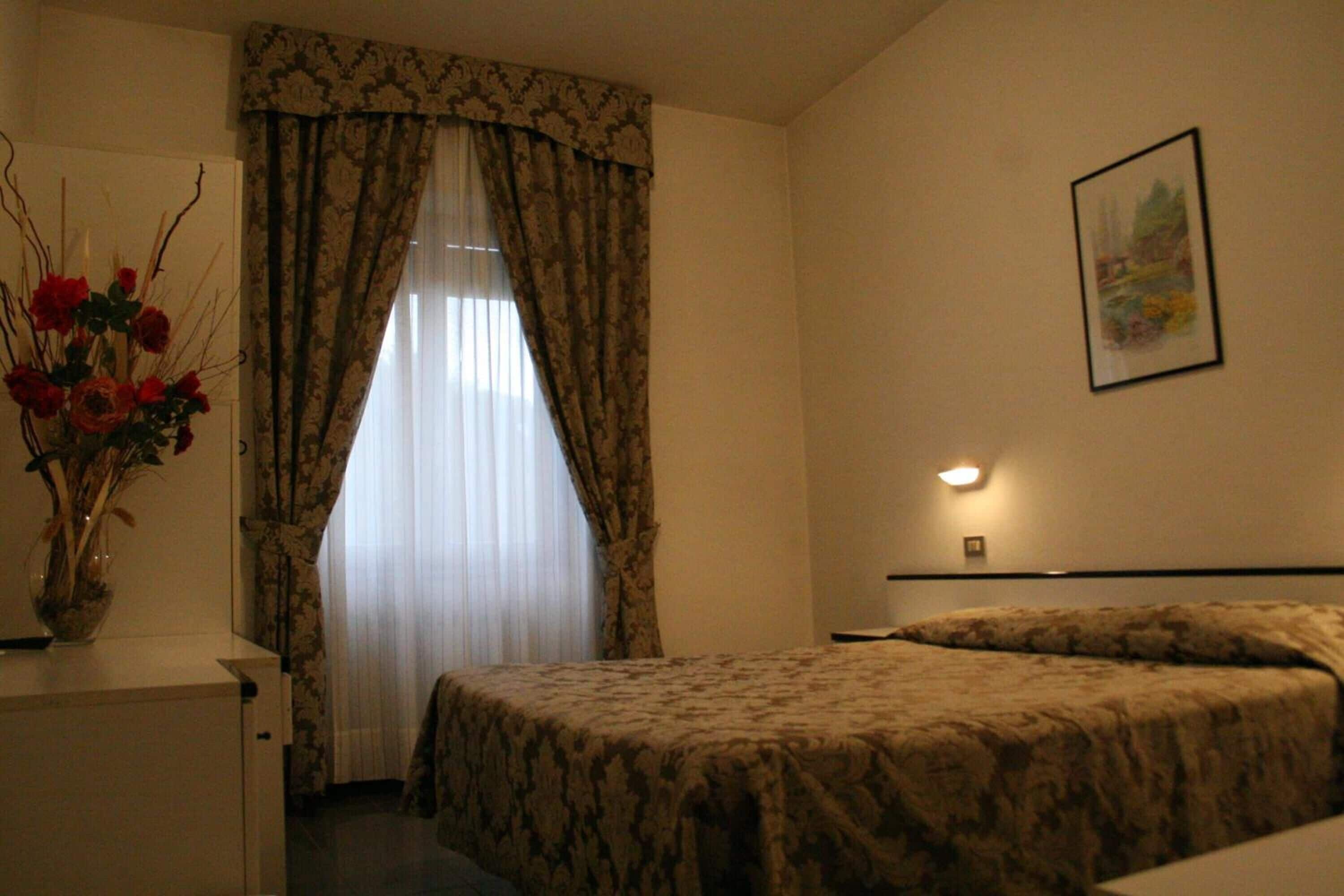 Ein Hotelzimmer mit einem Bett, einem Nachttisch, einer Vase mit Blumen und einem Gemälde an der Wand.