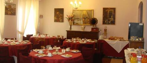 Un comedor con mesas redondas cubiertas de manteles rojos, vajilla blanca y sillas.