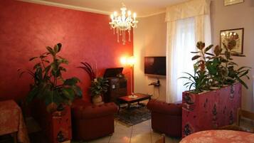 A living room with red walls, a chandelier, a sofa set, a TV, and two potted plants.