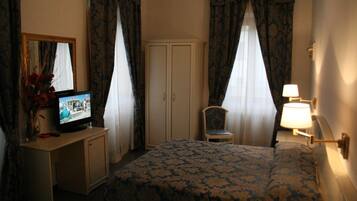Habitación de hotel con cama, televisión sobre una mesita, una silla, armario y cortinas.