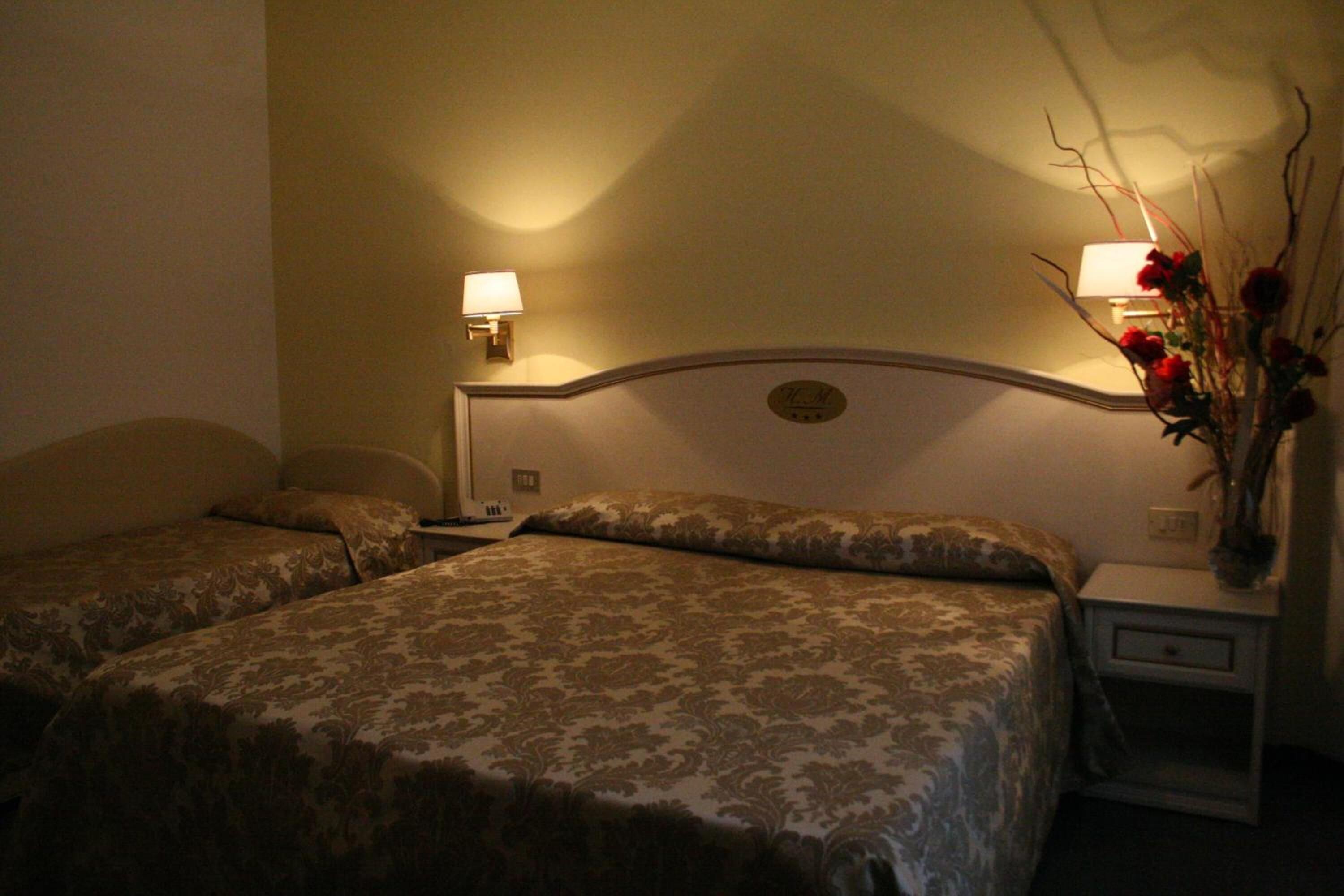 Une chambre d’hôtel avec deux lits, chacun recouvert d’une couvre-lit à motifs, une table de chevet avec une lampe et un vase rempli de fleurs.