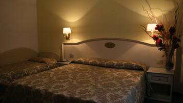 Une chambre d’hôtel avec deux lits, chacun recouvert d’une couvre-lit à motifs, une table de chevet avec une lampe et un vase rempli de fleurs.