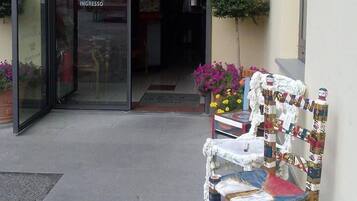 Entrada de un restaurante con puerta de cristal, un pequeño espacio exterior con una silla y plantas en macetas.