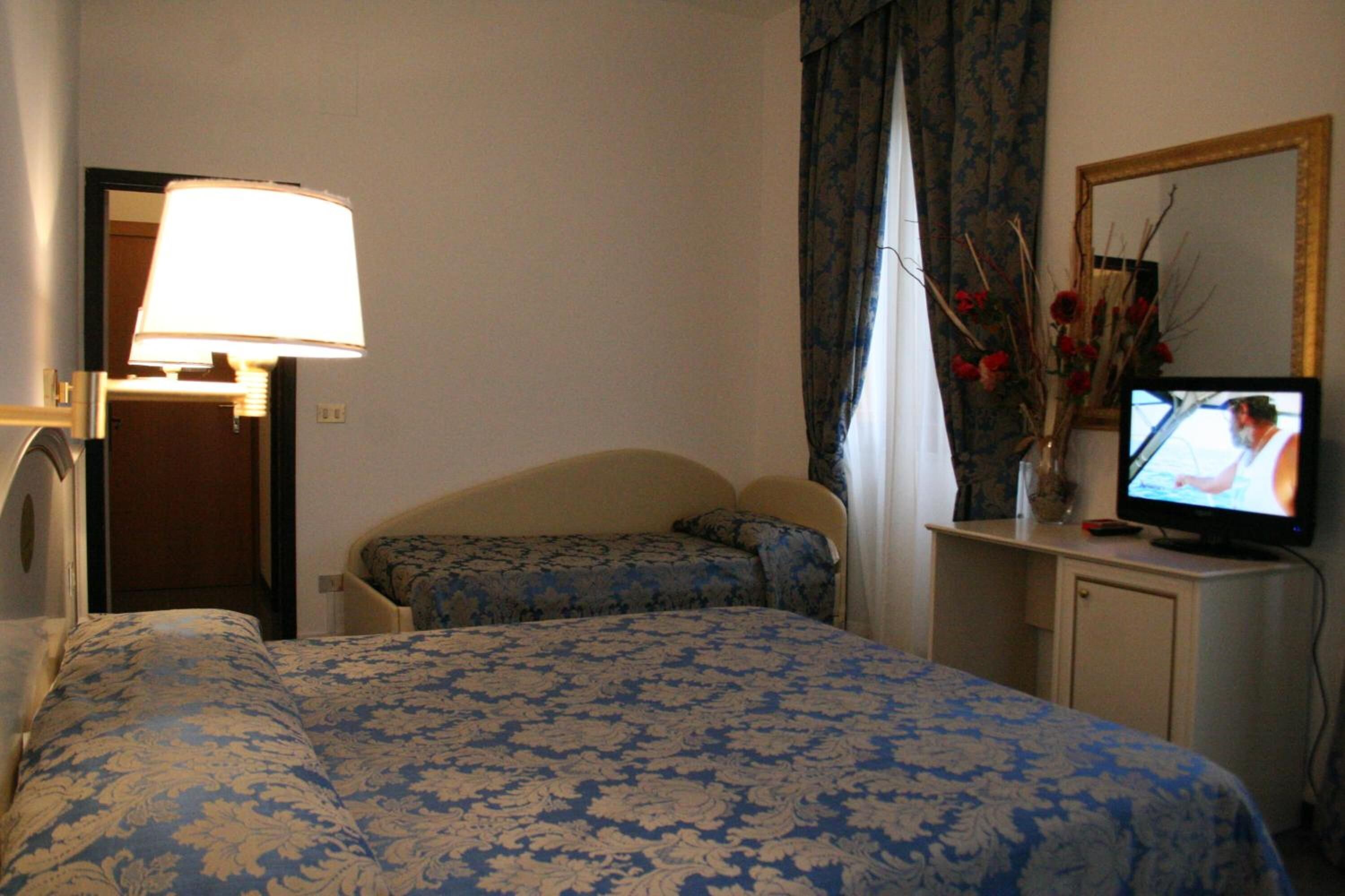 A hotel room with a bed, a desk with a television, a lamp, and a mirror.