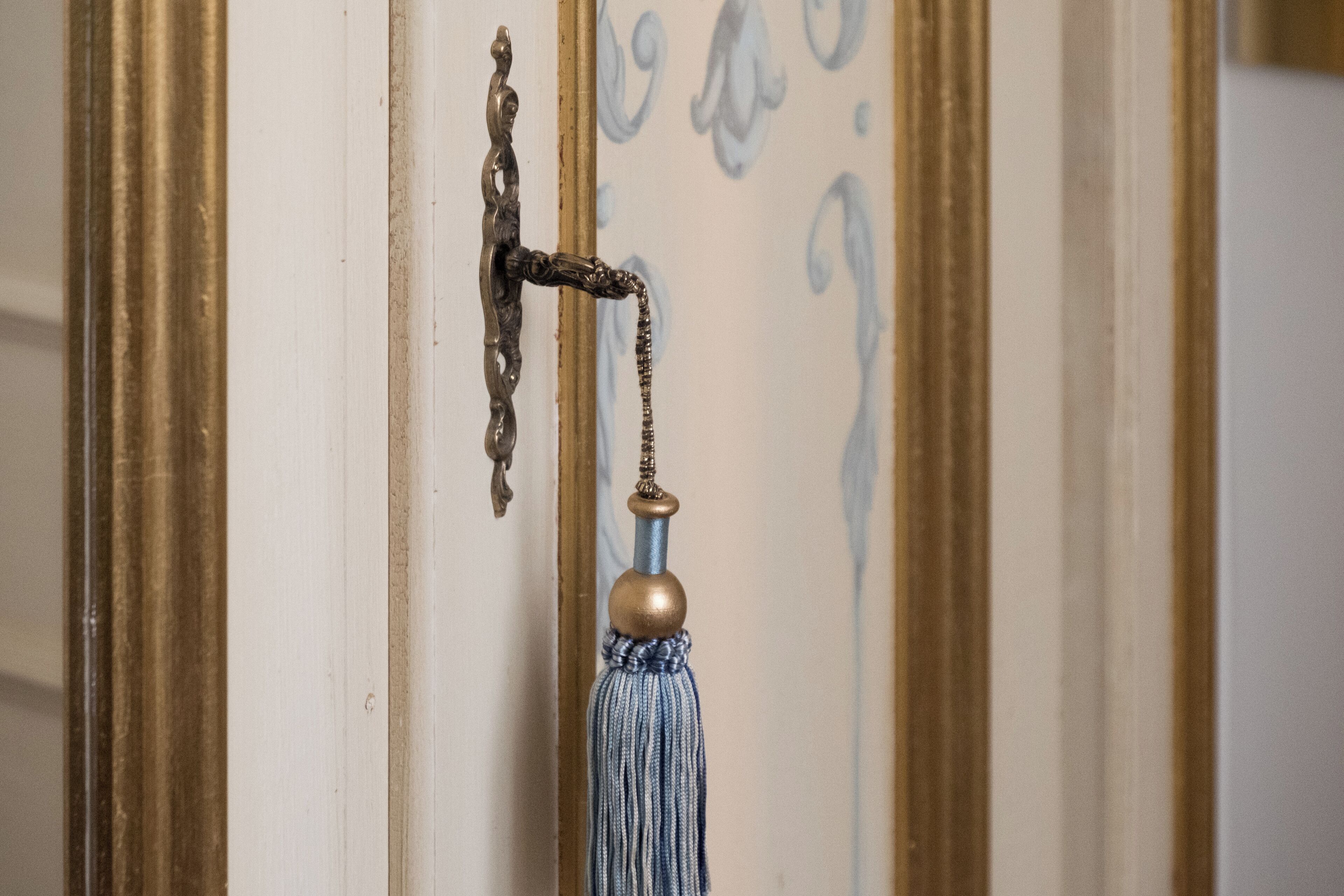 A door with an ornate brass handle and a blue tassel hanging from it.