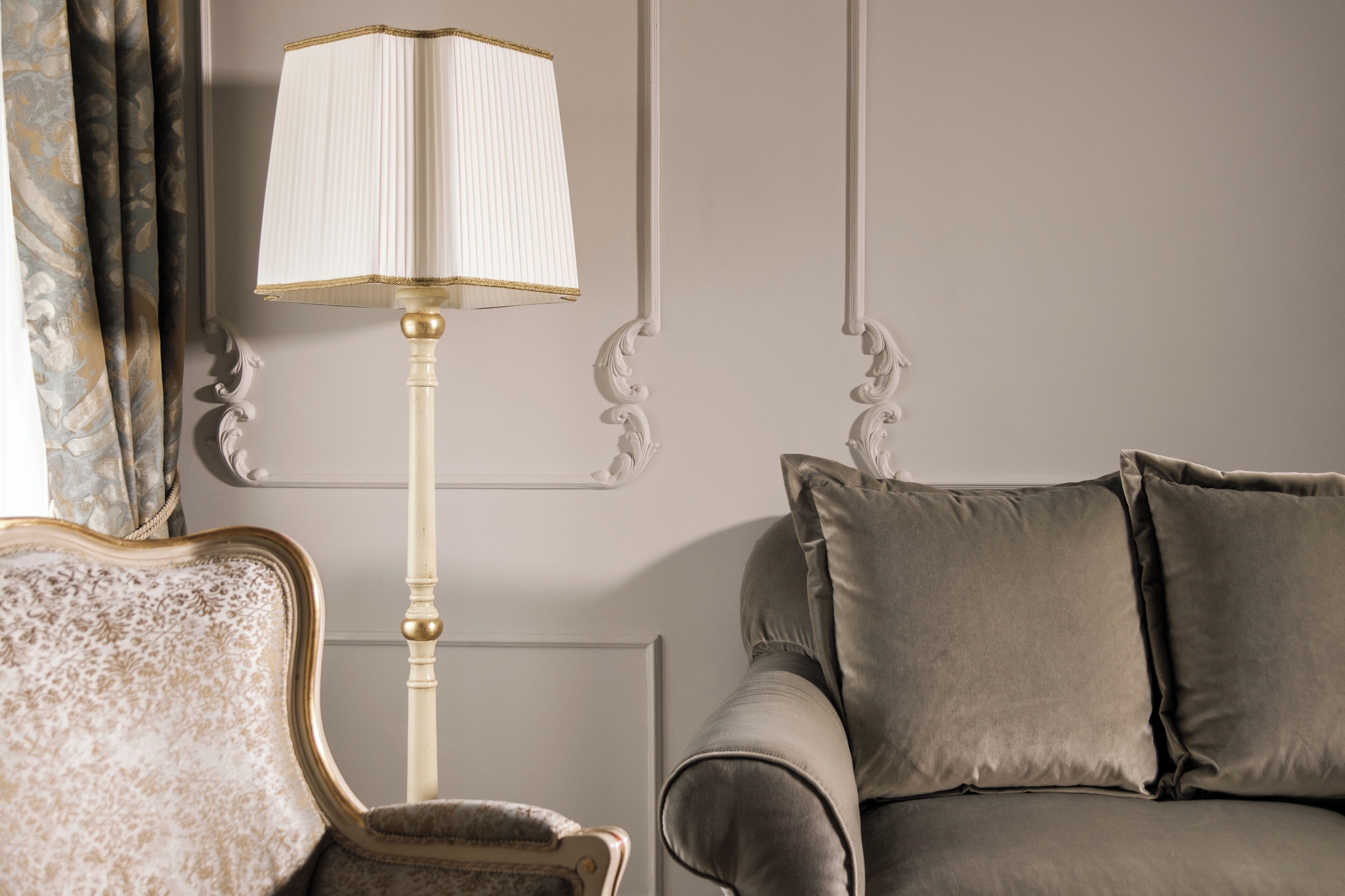A room with a classic lamp, a sofa, and a chair with ornate detailing.