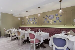 Un restaurante con mesas y sillas blancas, un banco con cojines rojos y platos decorativos azul y blanco en la pared.
