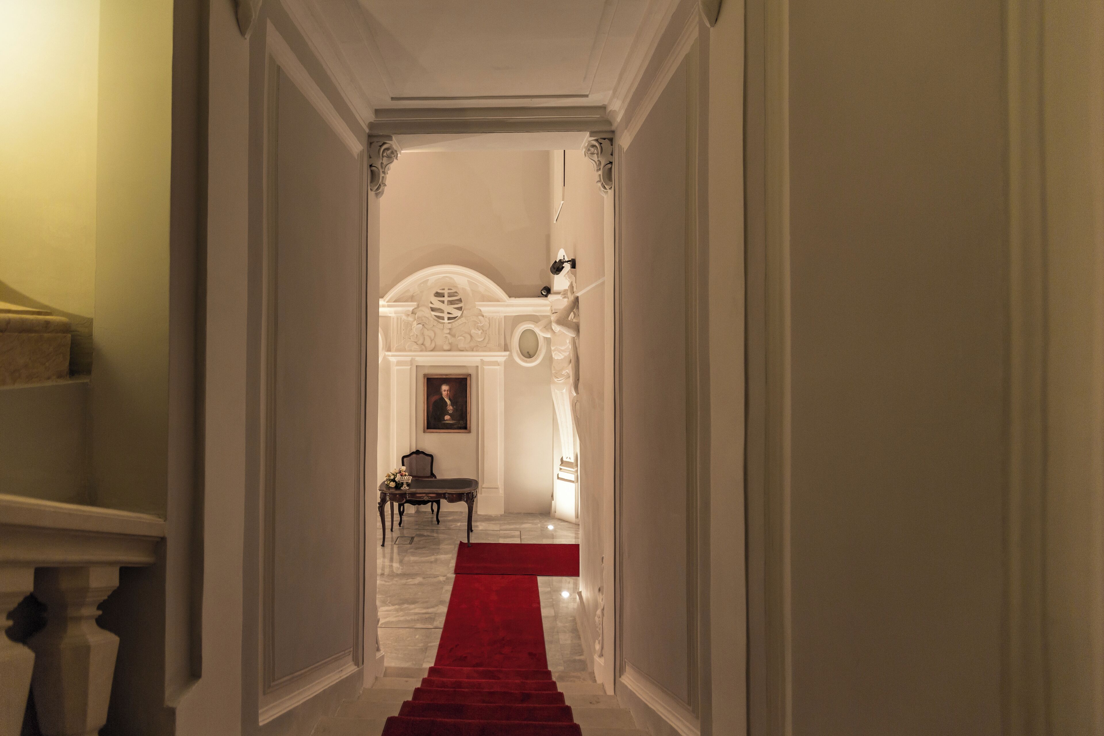 Un pasillo con alfombra roja que conduce a una habitación con cama y mesita de noche.