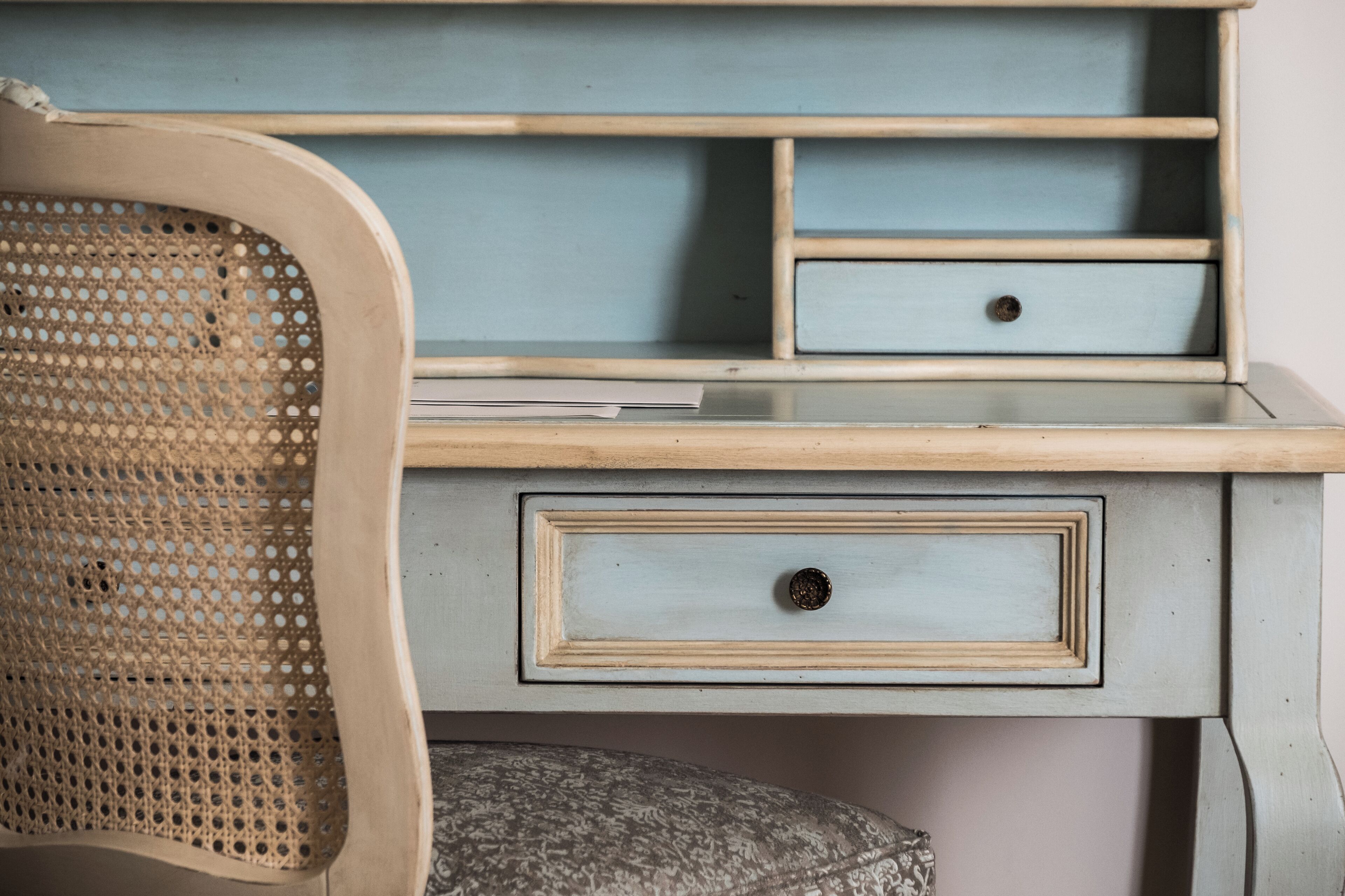 A vintage-style desk with a rattan chair, featuring drawers and shelves.