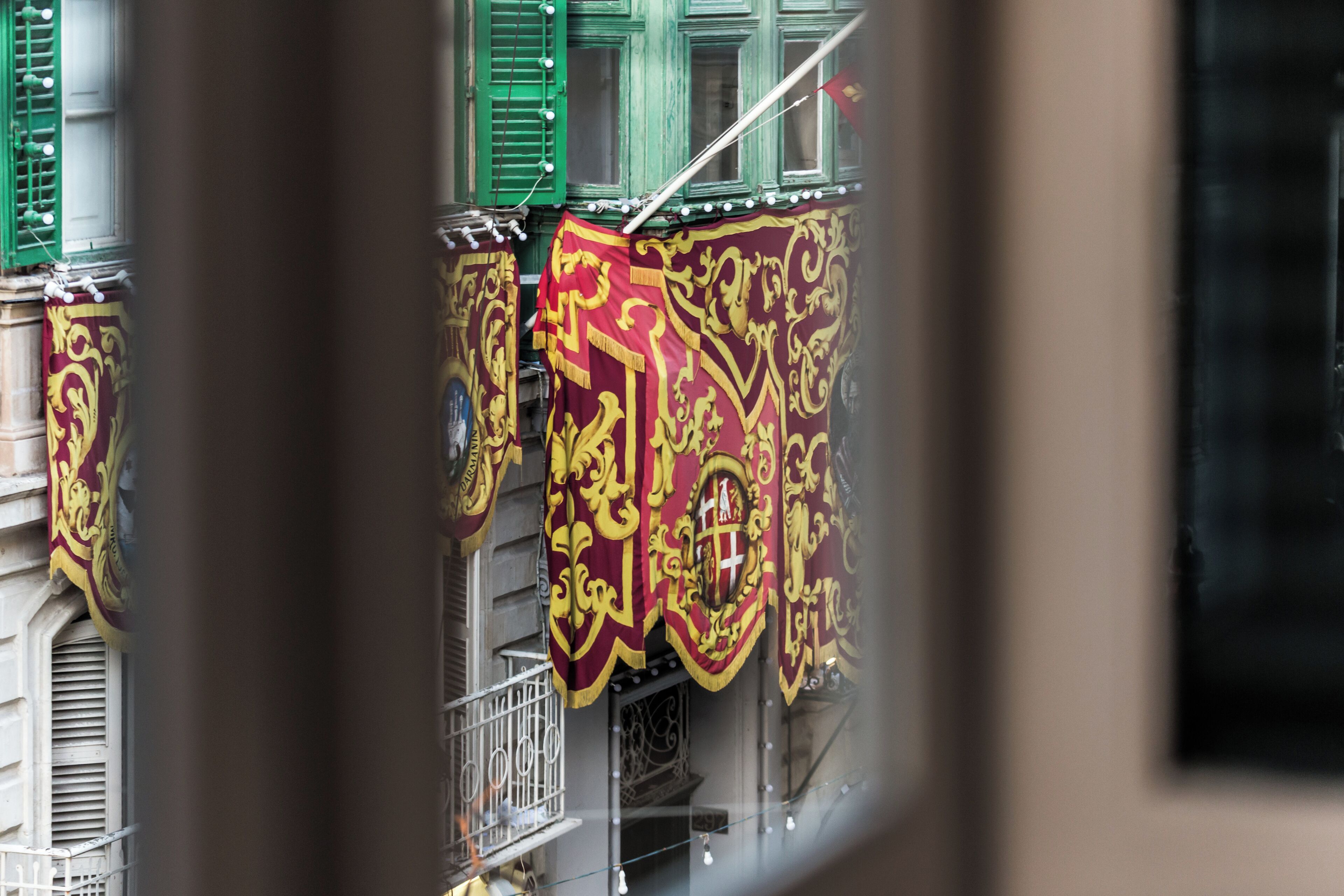 A building facade with green shutters and ornate red and gold banners.