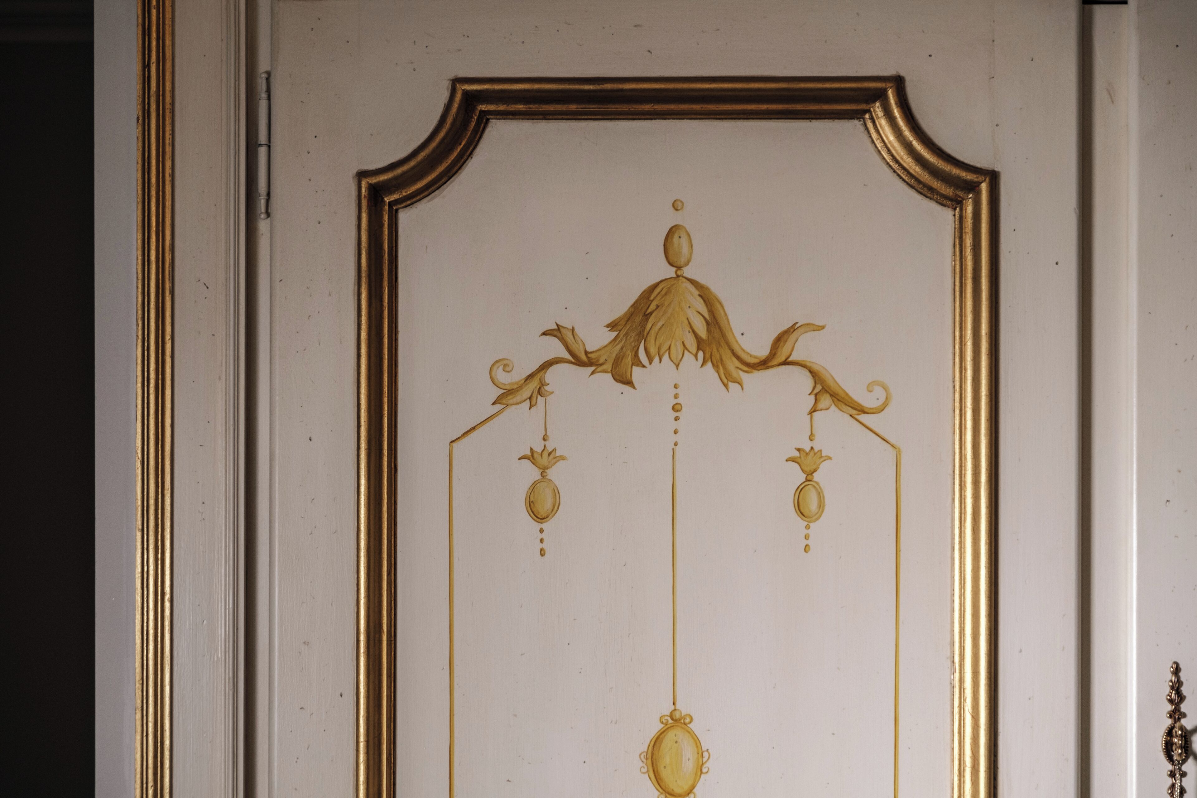 A door with a gold-colored ornate design, including a central hanging ornament and two smaller hanging ornaments.