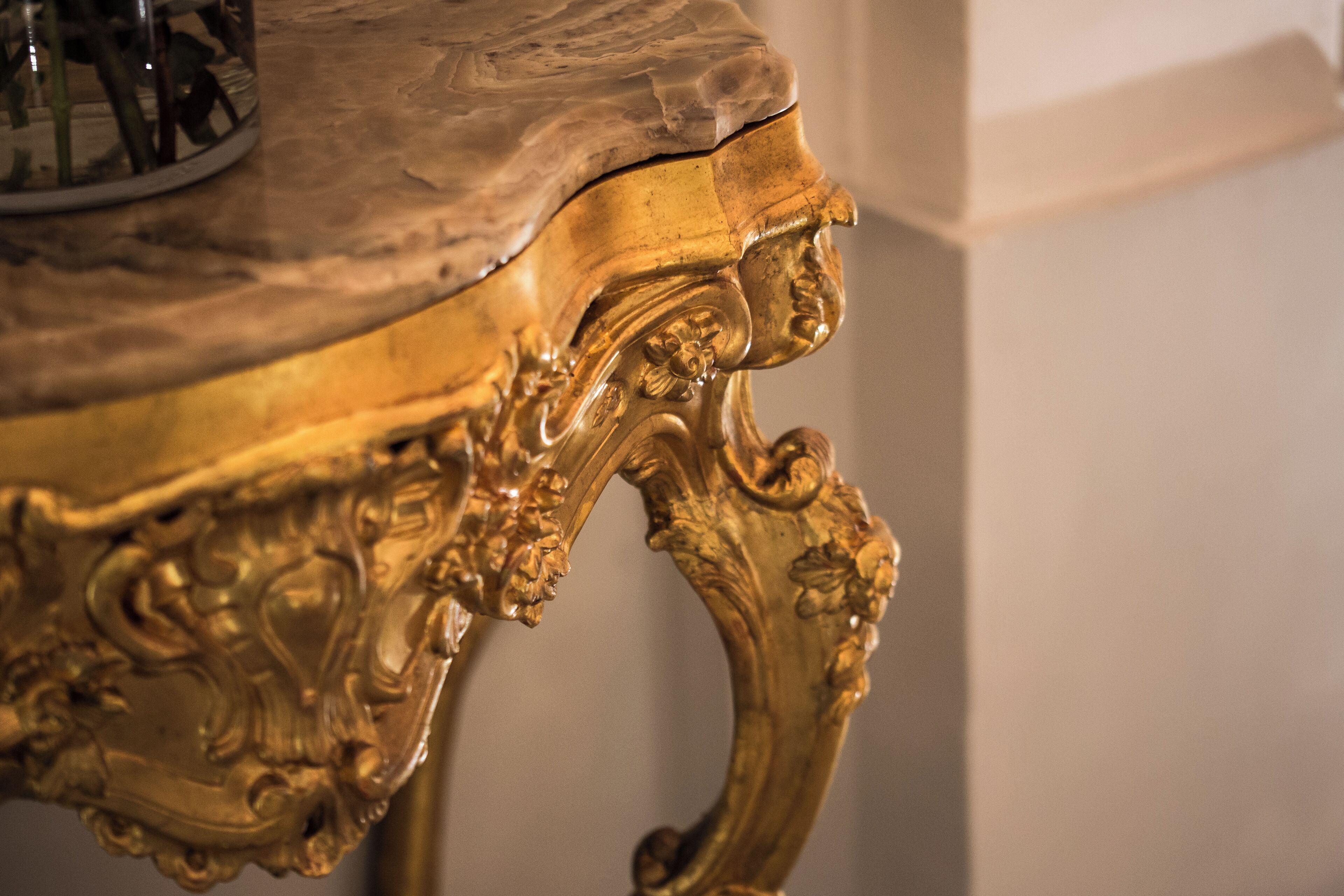 A close-up of an ornate, gold-colored table with intricate carvings and a marble top.