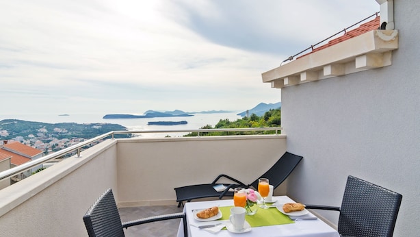 A balcony with a table set for breakfast, overlooking a scenic view of a body of water and distant mountains. - Apartments Villa Dadic (Dubrovnik)