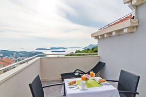 A balcony with a table set for breakfast, overlooking a scenic view of a body of water and distant mountains.