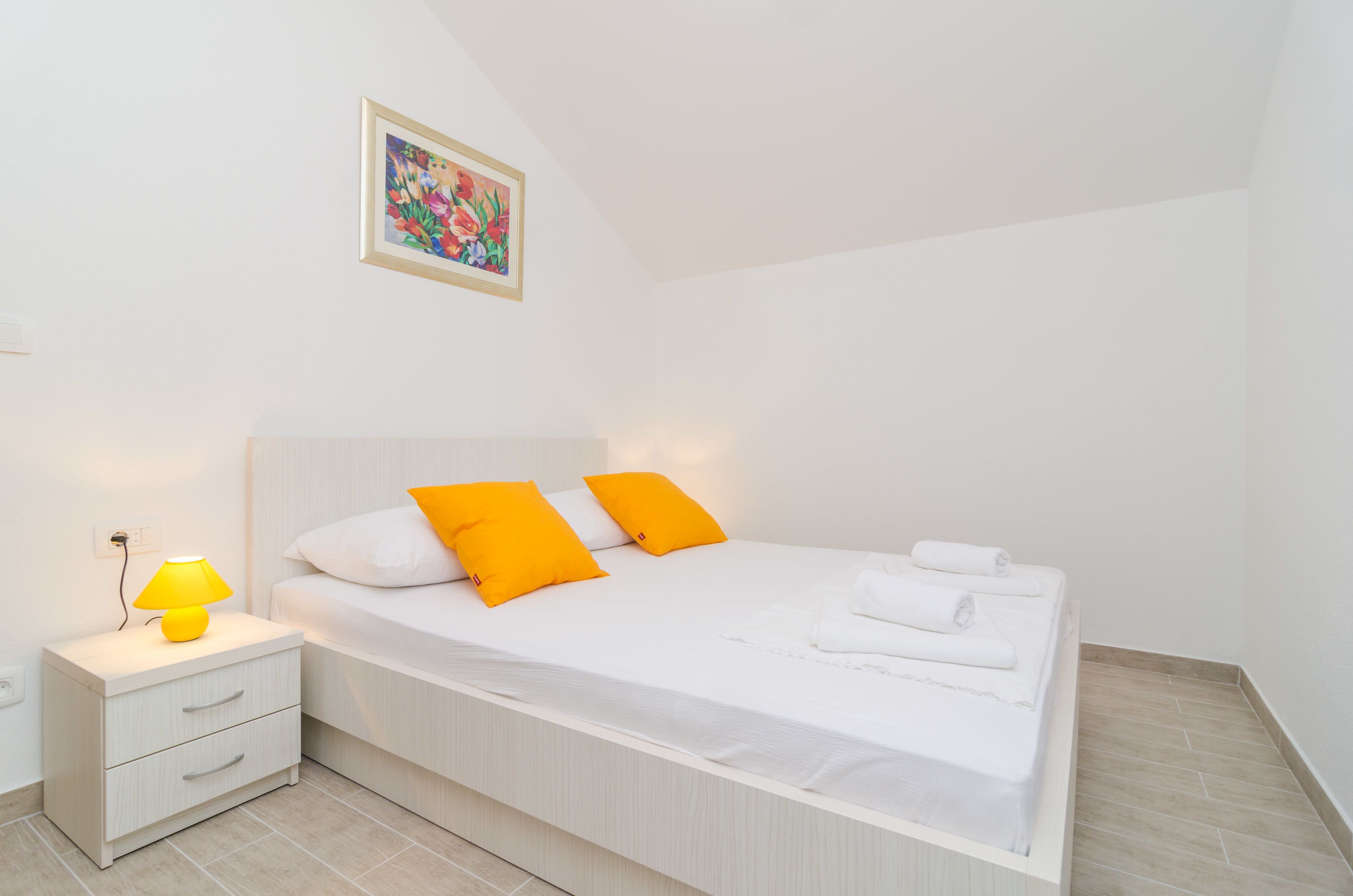 Een netjes opgemaakt slaapkamer met een bed, nachtkastje met een lamp en een aan de muur hangend schilderij.