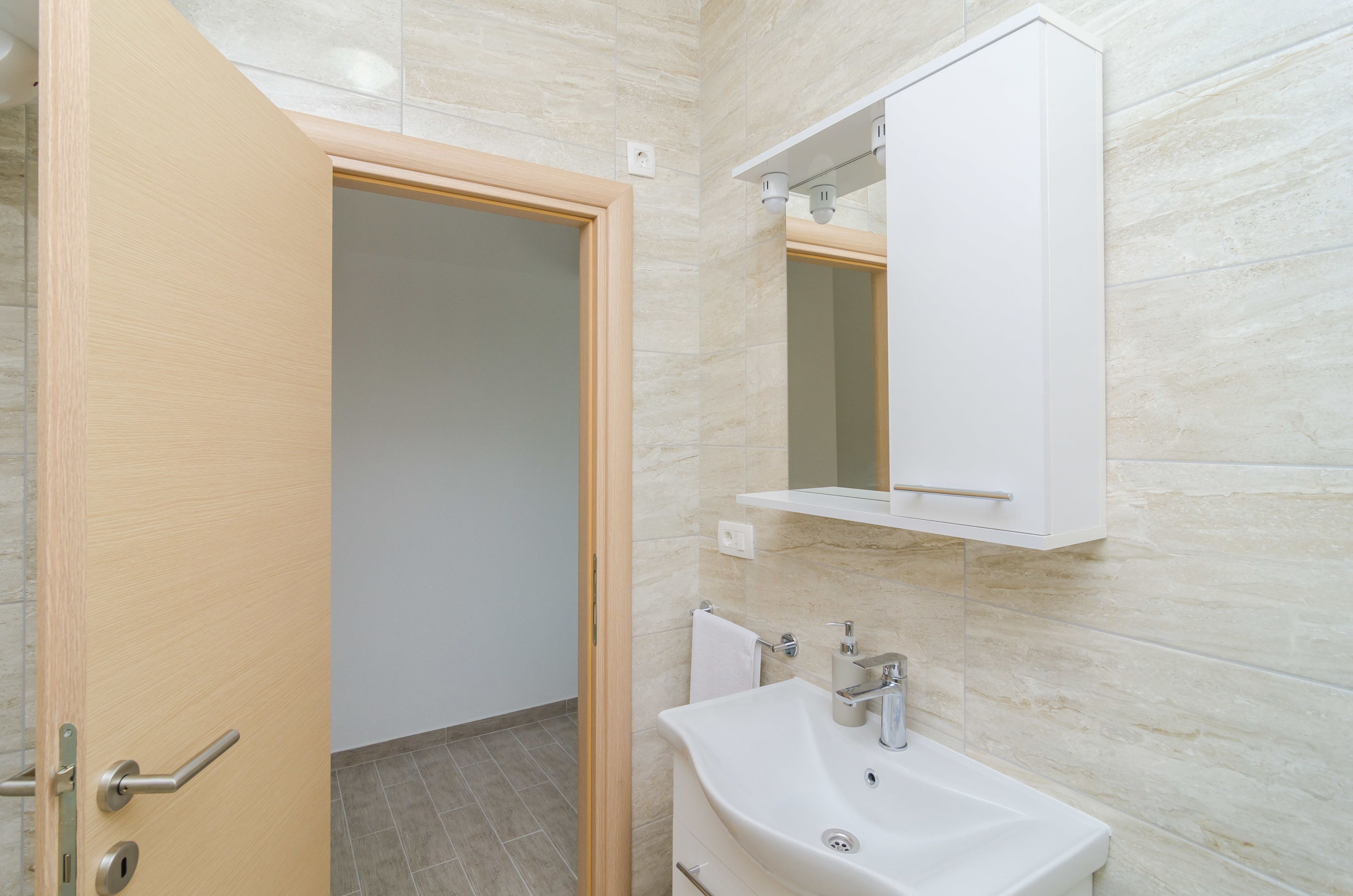 A bathroom with a wooden door, a white sink, and a mirror above it.