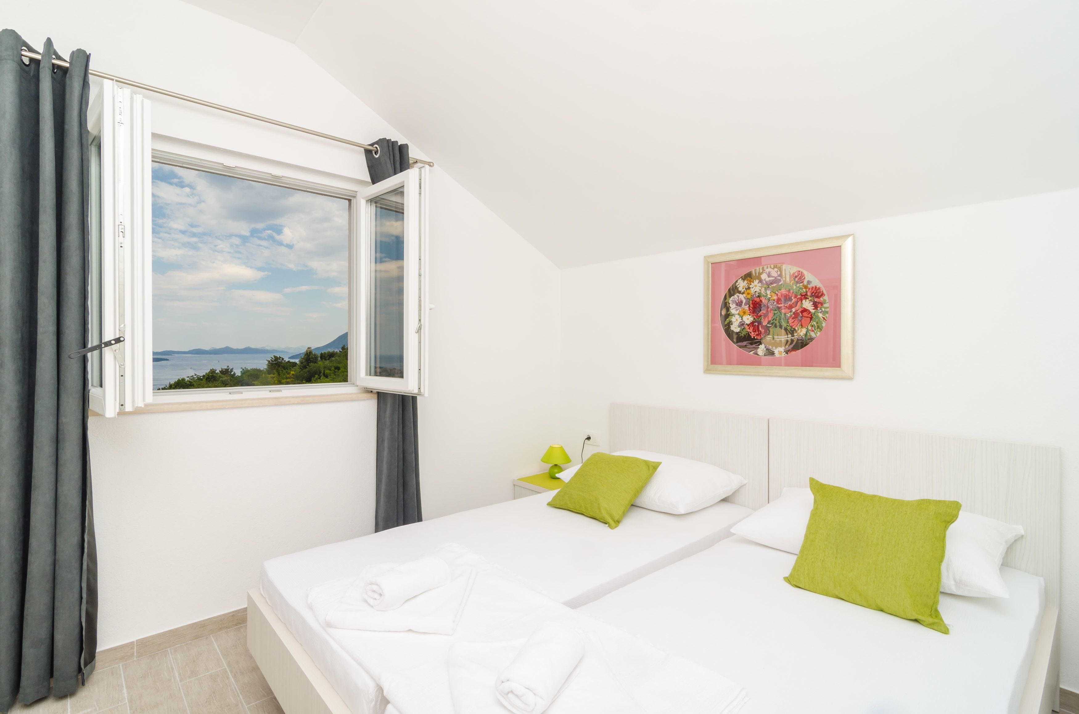 Une chambre avec deux lits, une fenêtre avec des rideaux, une table de chevet avec une lampe et une œuvre d’art florale encadrée accrochée au mur.