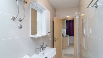 Un baño moderno con lavamanos, espejo y ducha blancos.
