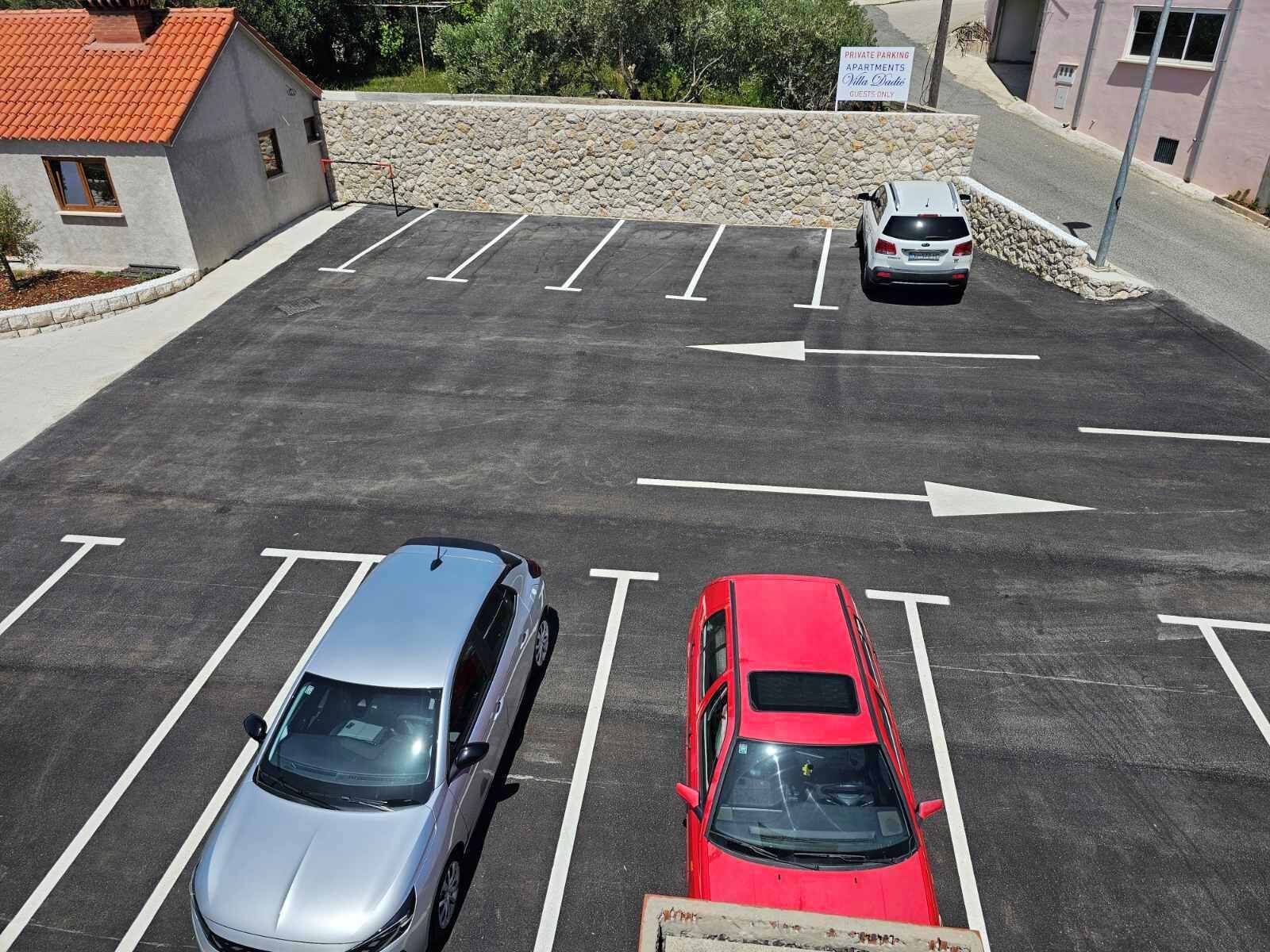 Een parkeerplaats met twee auto's, een bord dat aangeeft dat het parkeren gereserveerd is voor gasten, en een stenen muur op de achtergrond.