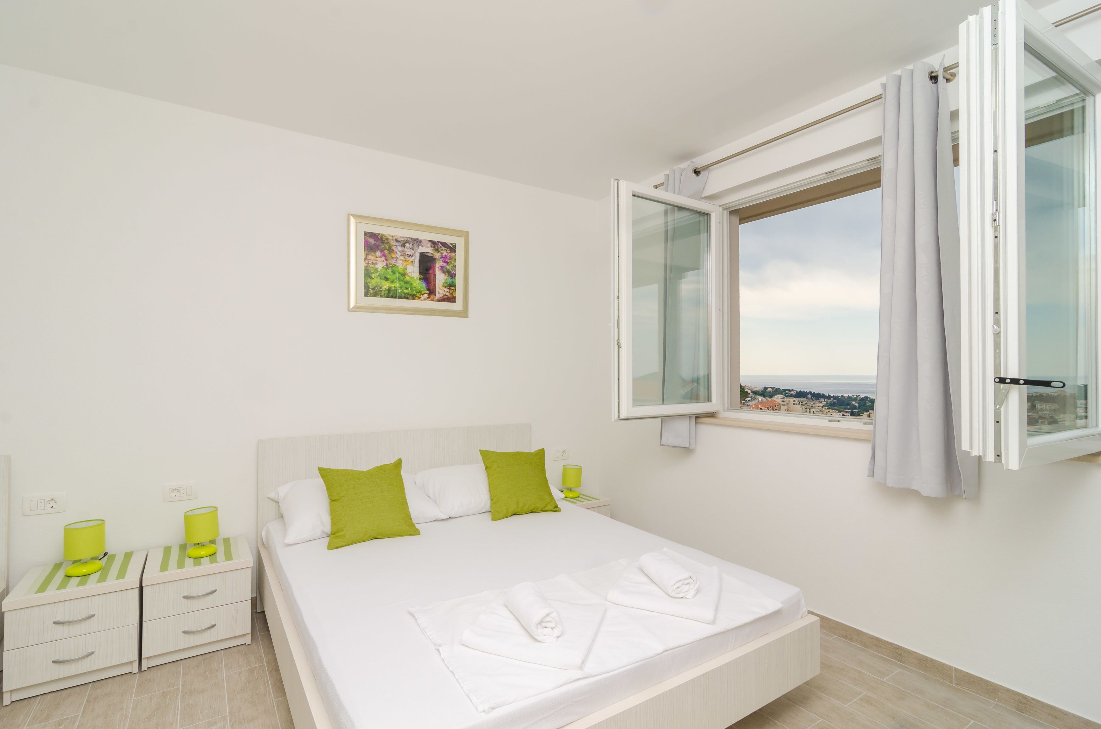 A bedroom with a bed, two bedside tables, a window with curtains, and a wall-mounted picture.