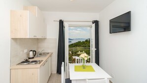 A compact kitchen with a view of the outdoors, a dining area with a table and chairs, and a flat-screen TV mounted on the wall. - Apartments Villa Dadic (Dubrovnik)