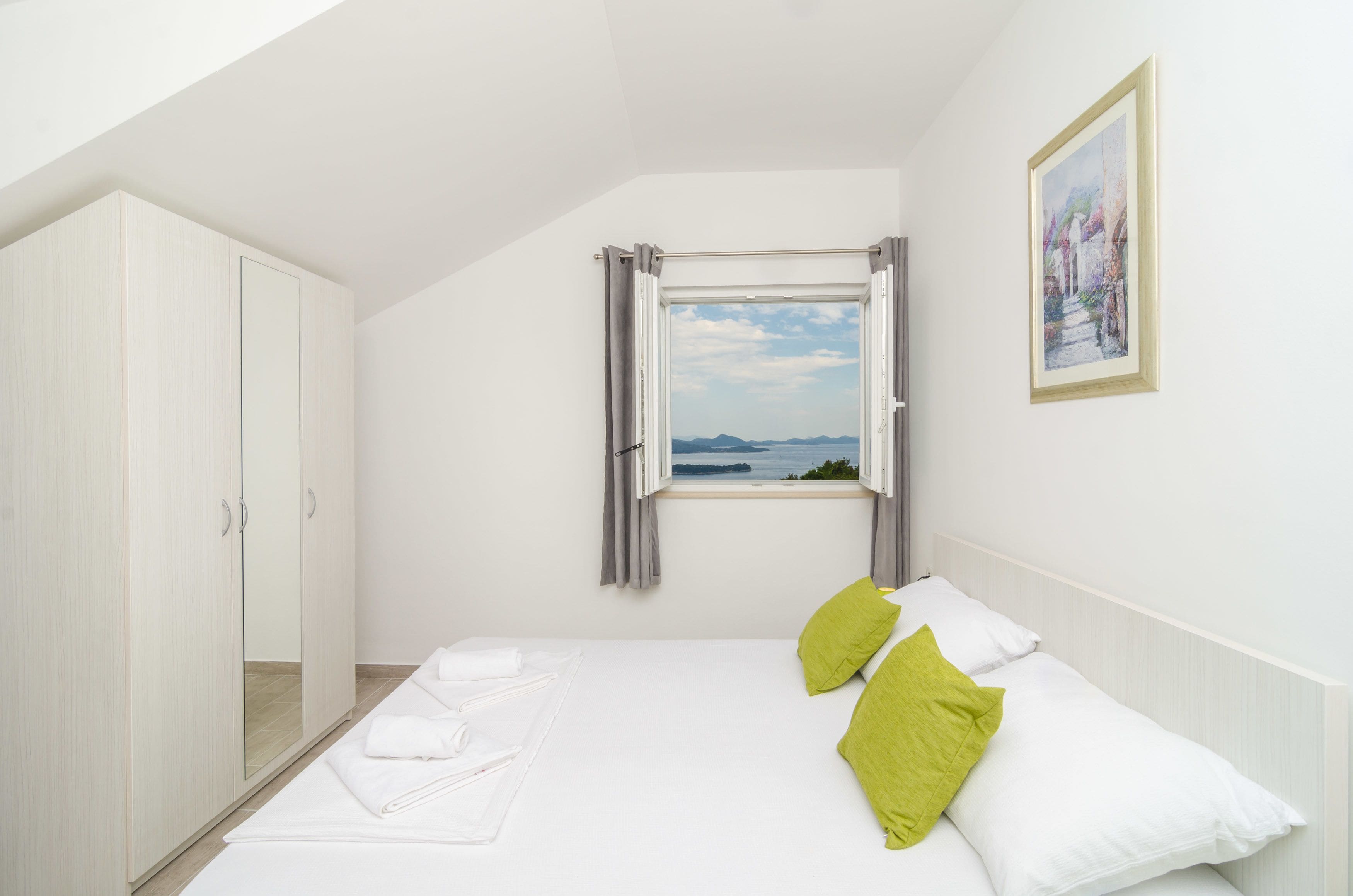 A bedroom with a bed, a window with curtains, a wardrobe, and a painting on the wall.