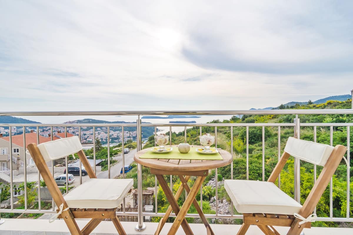 Een balkon met twee houten stoelen en een kleine ronde tafel met een groene mat.