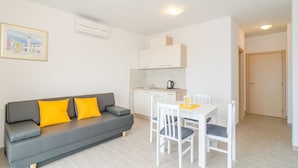 A compact living space with a grey sofa, white dining table, and chairs. A kitchen area with cabinets and a kettle is visible. - Apartments Villa Dadic (Dubrovnik)