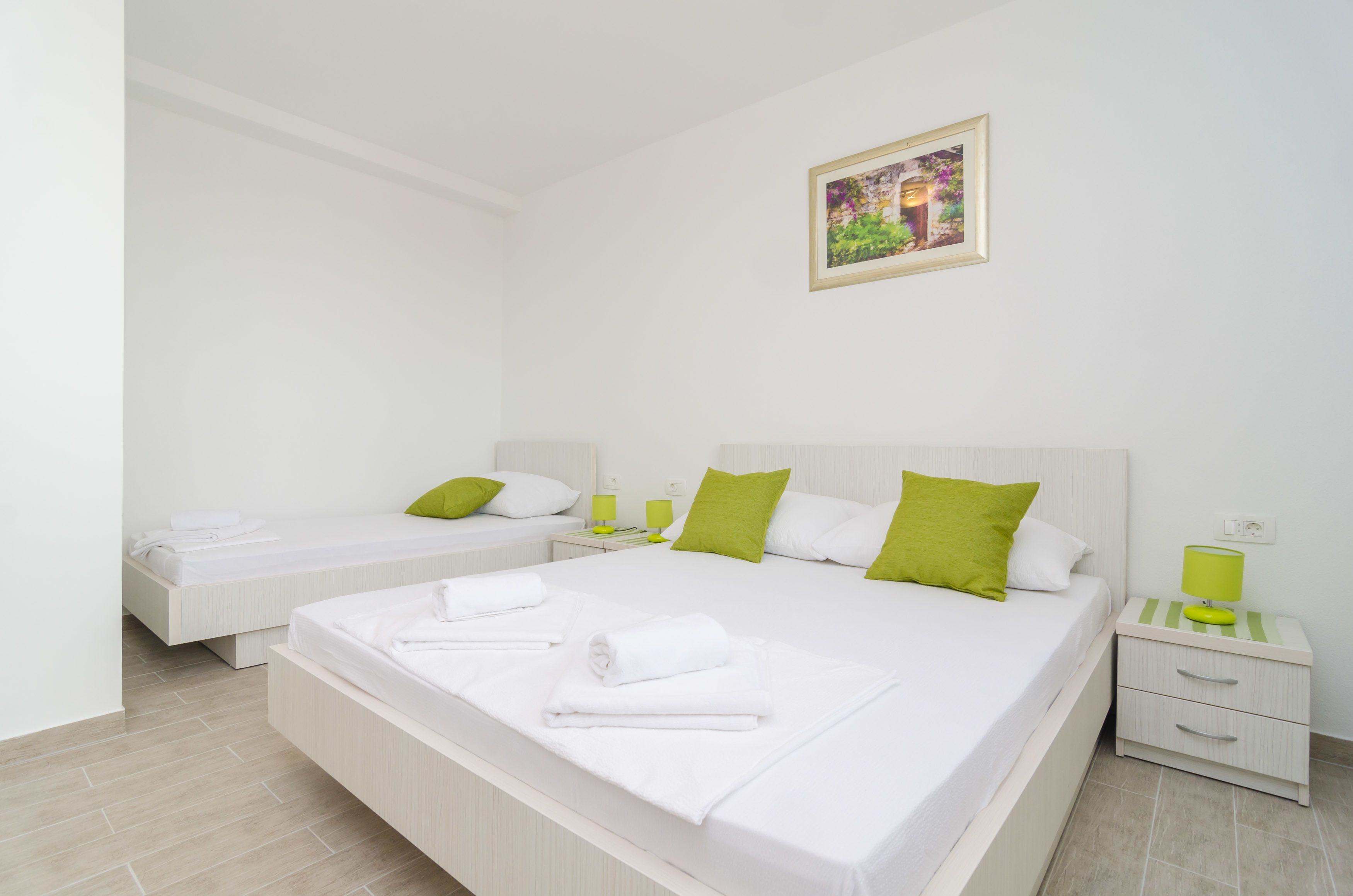 A hotel room with two single beds, a large bed, and a nightstand with a lamp.