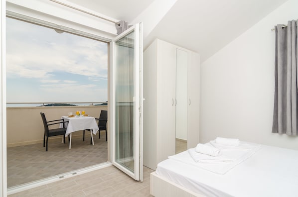 A bedroom with a balcony, a bed with white linens, a table with a white tablecloth, and a chair.