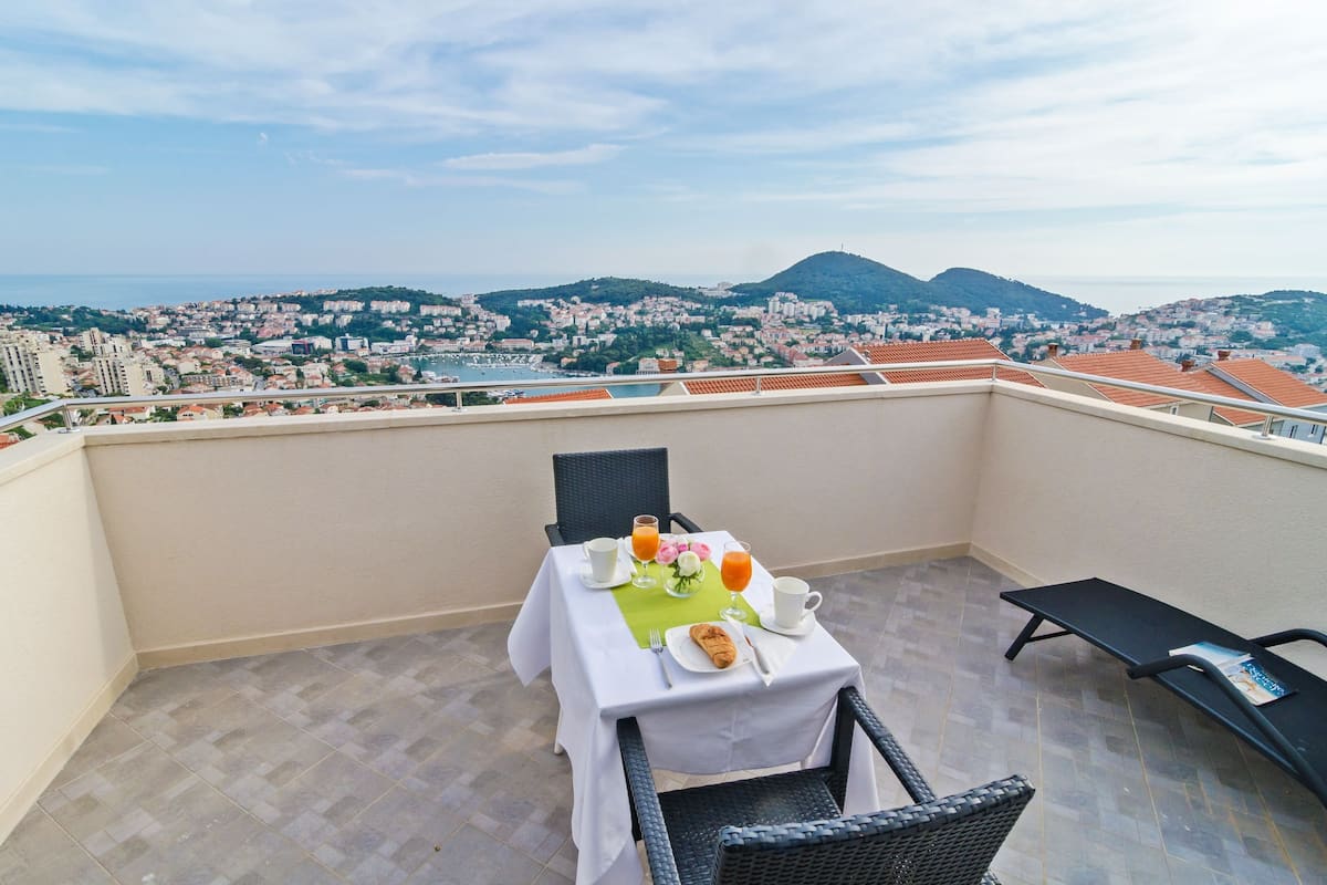 Een balkon met een ontbijtje erop, met uitzicht op een stadsgezicht met heuvels.