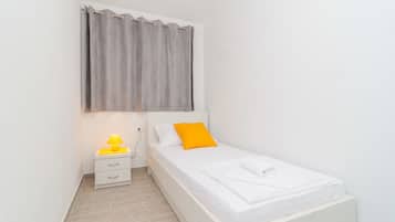 Un dormitorio pequeño y ordenado con una cama individual, una mesita de noche con lámpara y una ventana con cortinas.