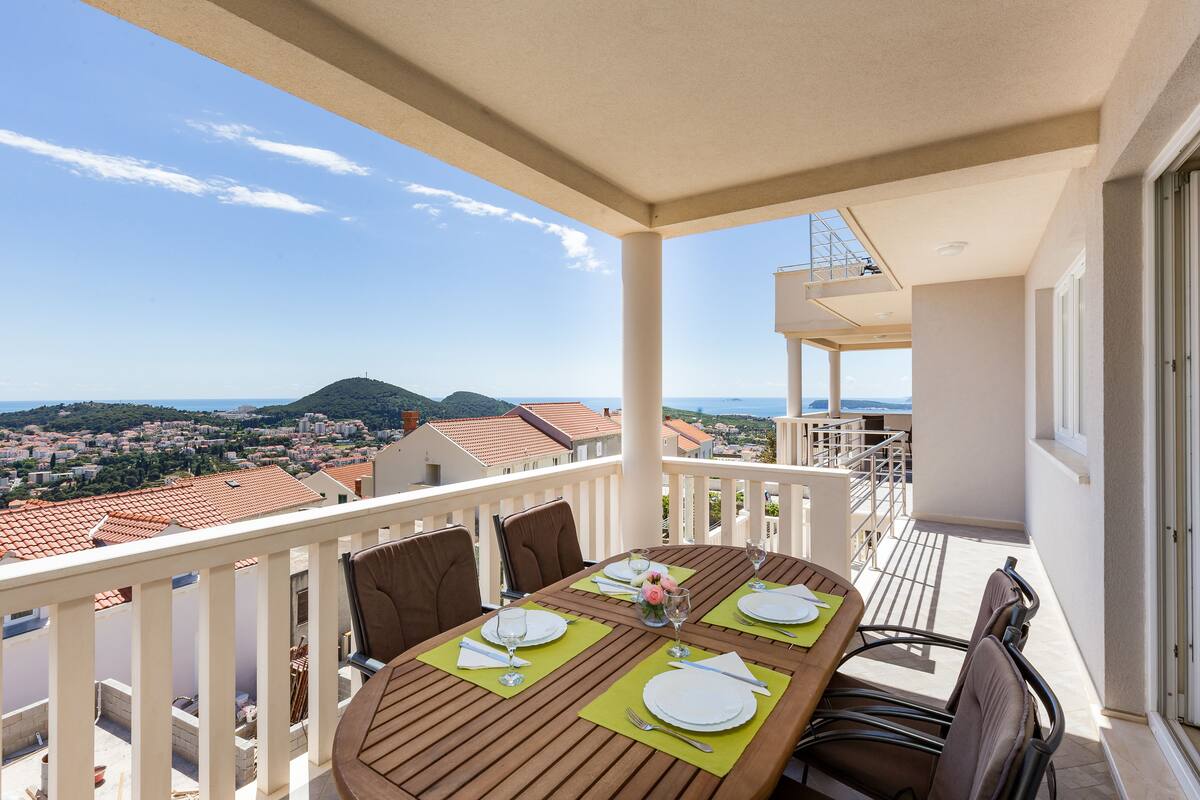 Een balkon met een tafel voor vier personen, met uitzicht op een stadsbeeld en heuvels.