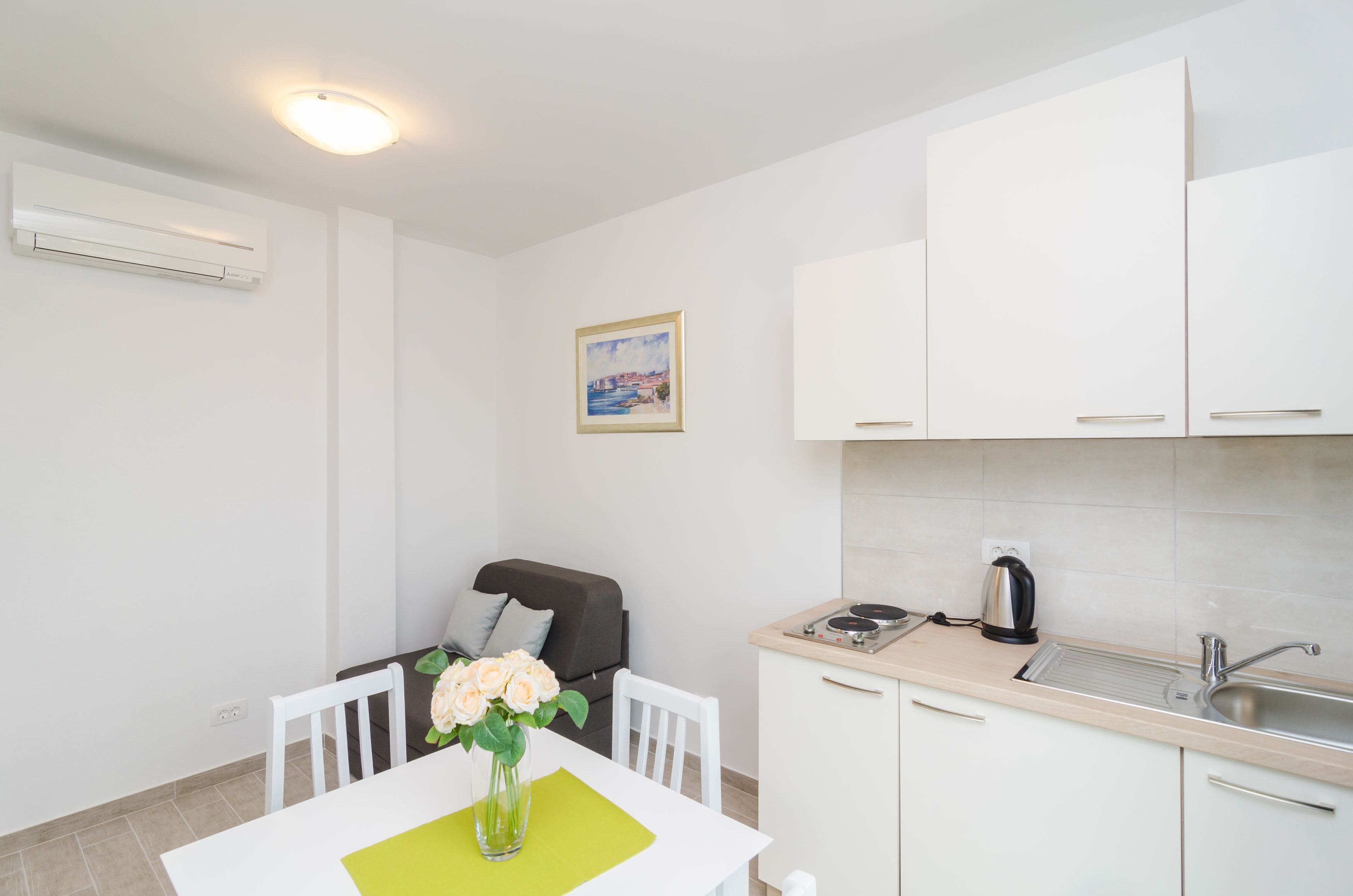 Una cocina moderna con armarios blancos, un fregadero y una estufa. Hay una mesa de comedor con sillas y un florero con flores.