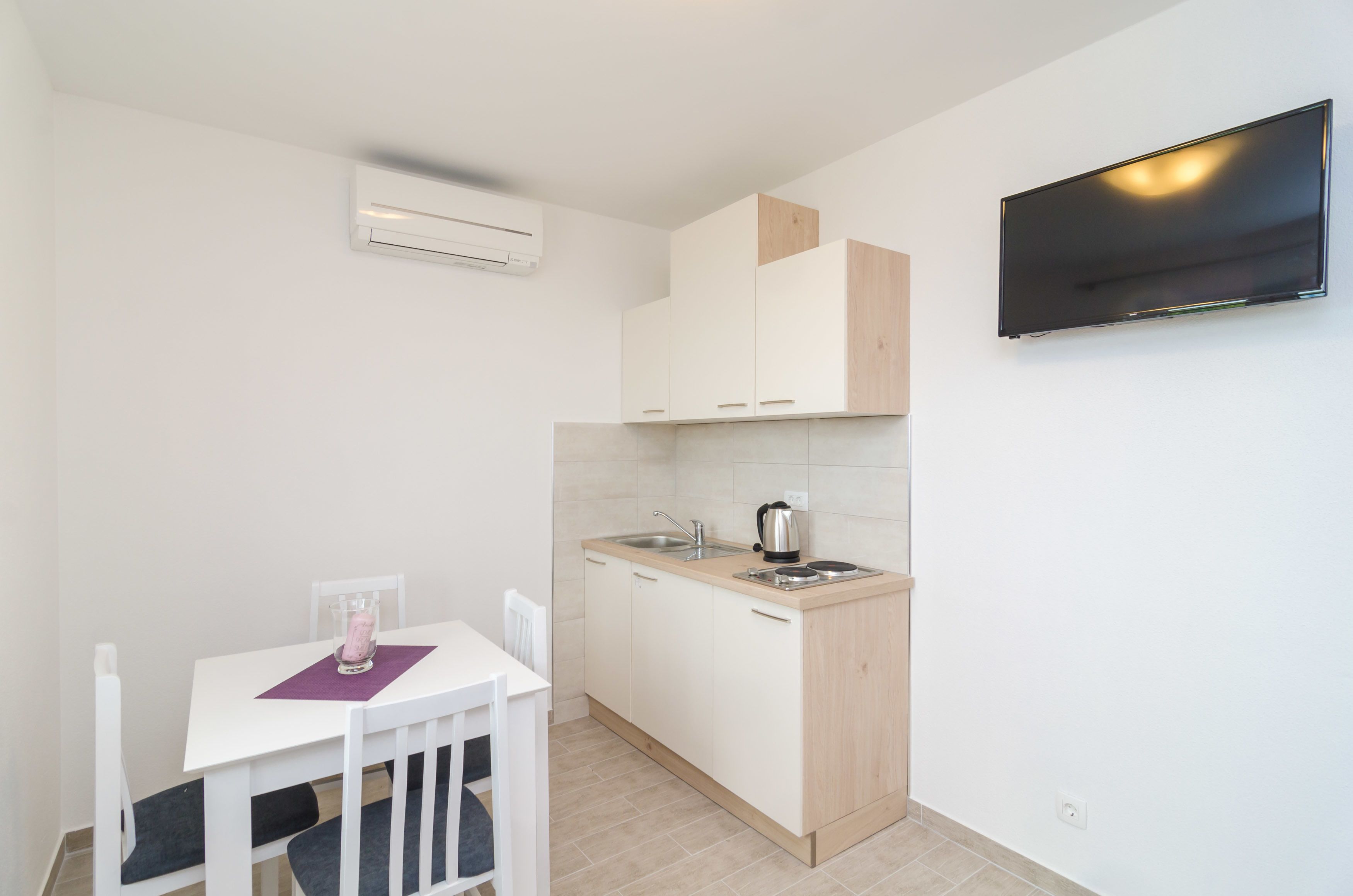 A compact kitchen with a white table, a single chair, a small sink, and a mounted TV.