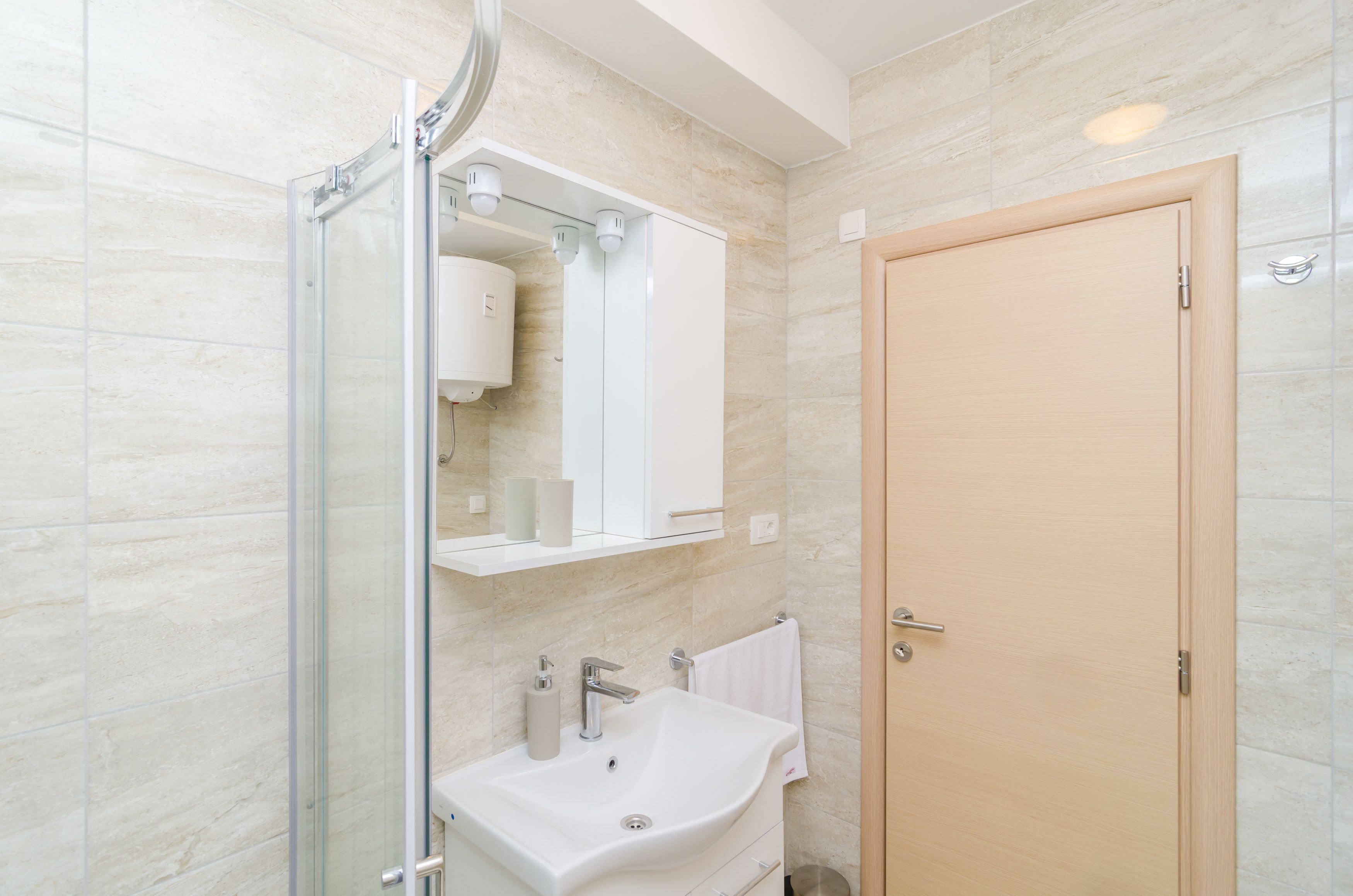 A modern bathroom with a glass shower enclosure, a white sink, and a wooden door.