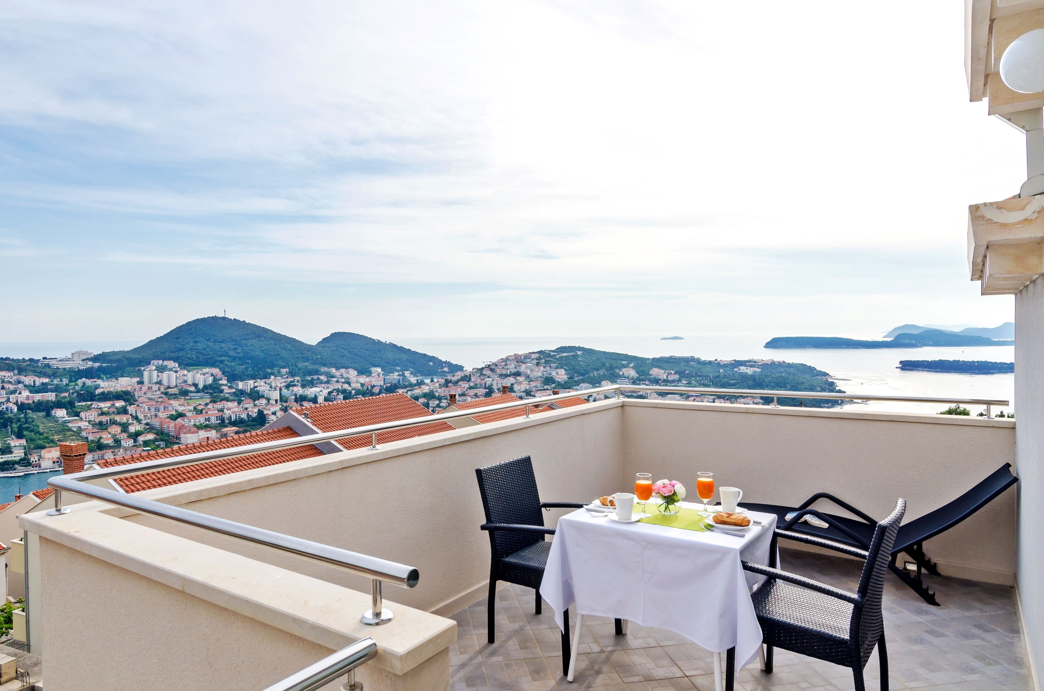 A balcony with a table set for breakfast, overlooking a coastal cityscape.