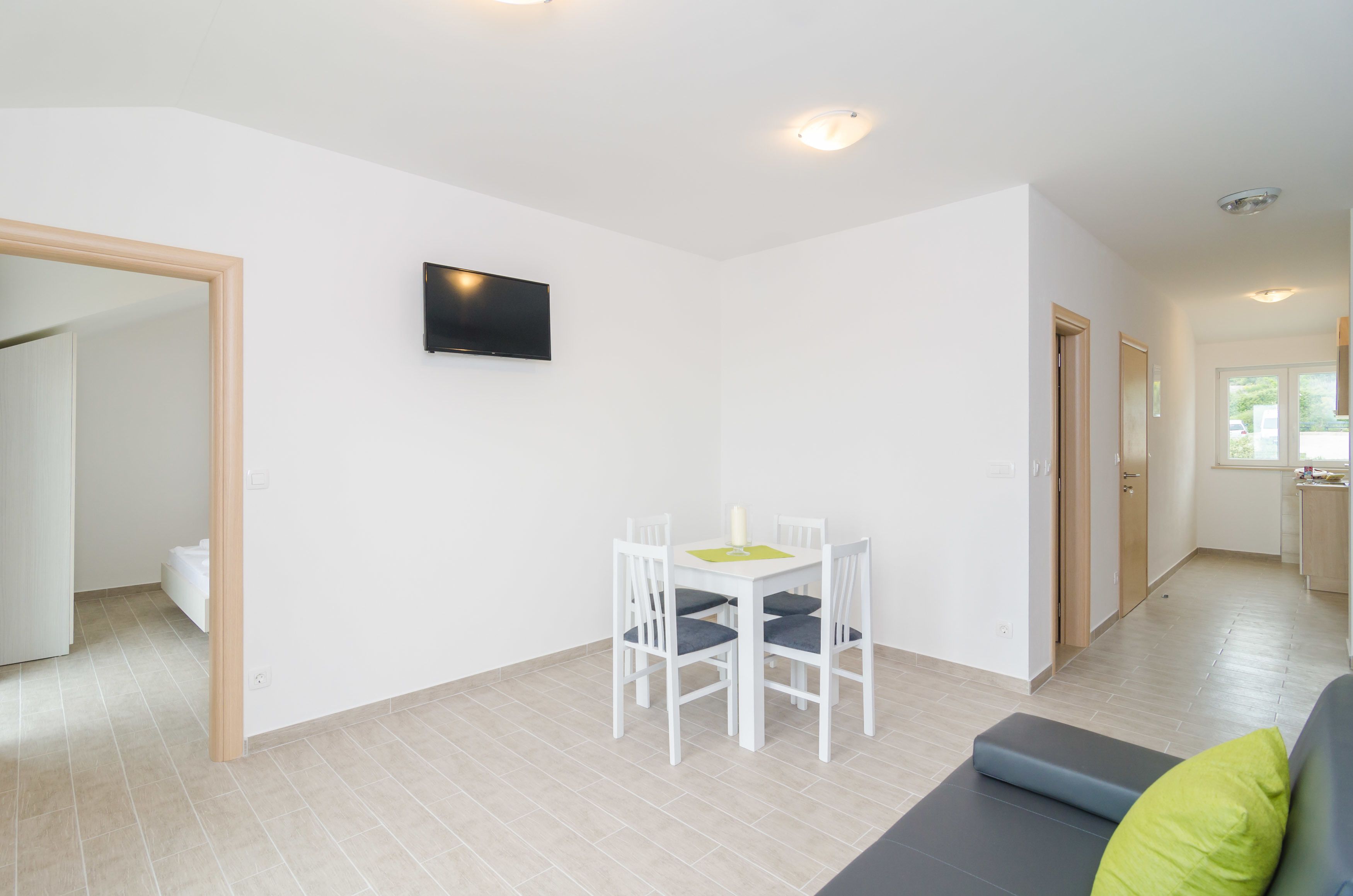 A modern living room with a dining area, a flat-screen TV mounted on the wall, and a sofa with a green cushion.