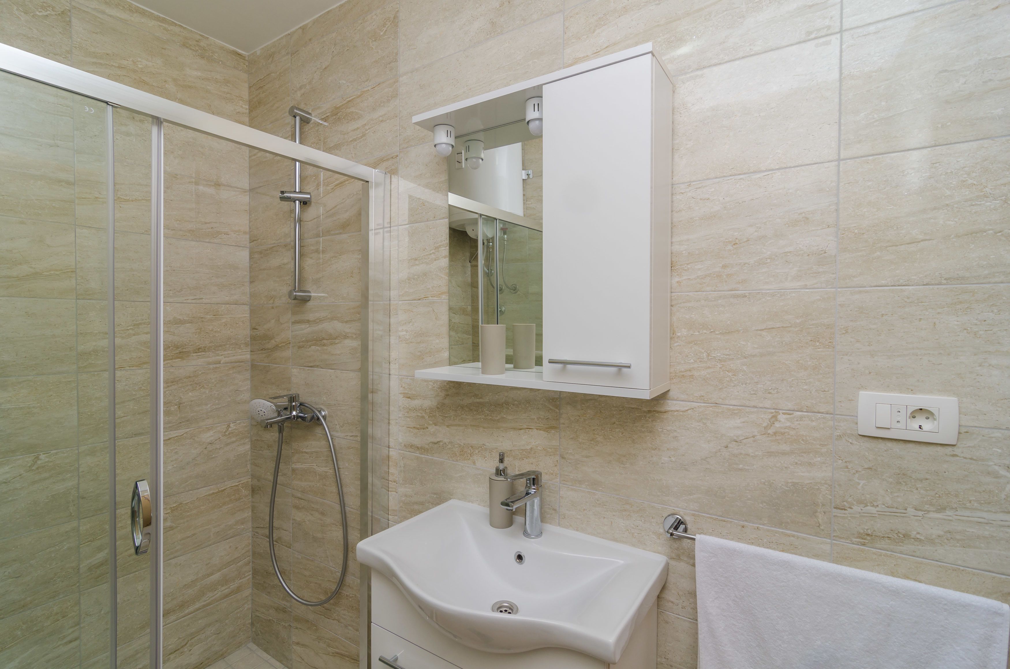 A modern bathroom with a glass-enclosed shower, a white sink, and a mirror above the sink.