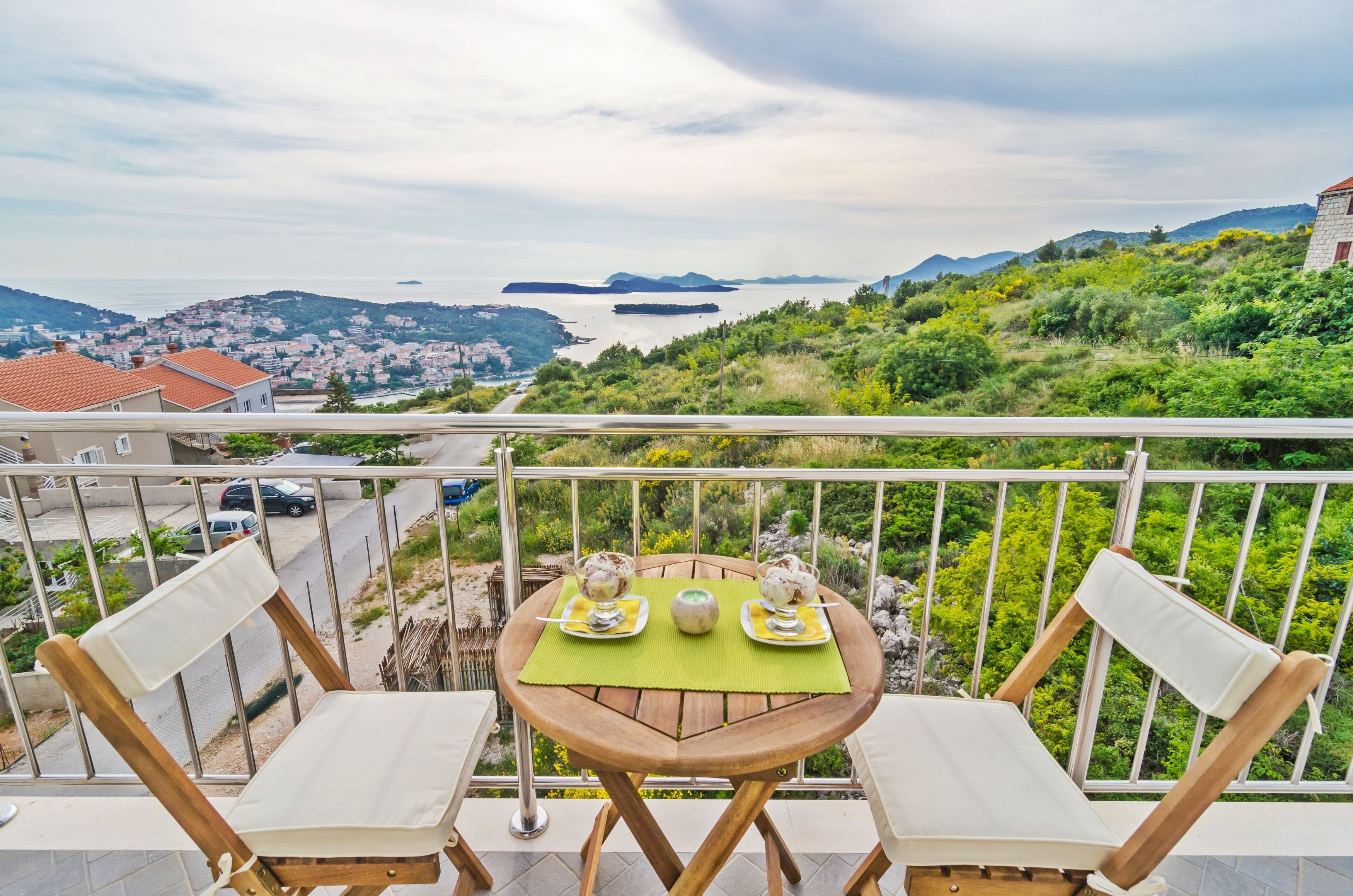 Ein Balkon mit Tisch für zwei Personen, mit Blick auf eine Küstenlandschaft mit Hügeln und einem Gewässer.