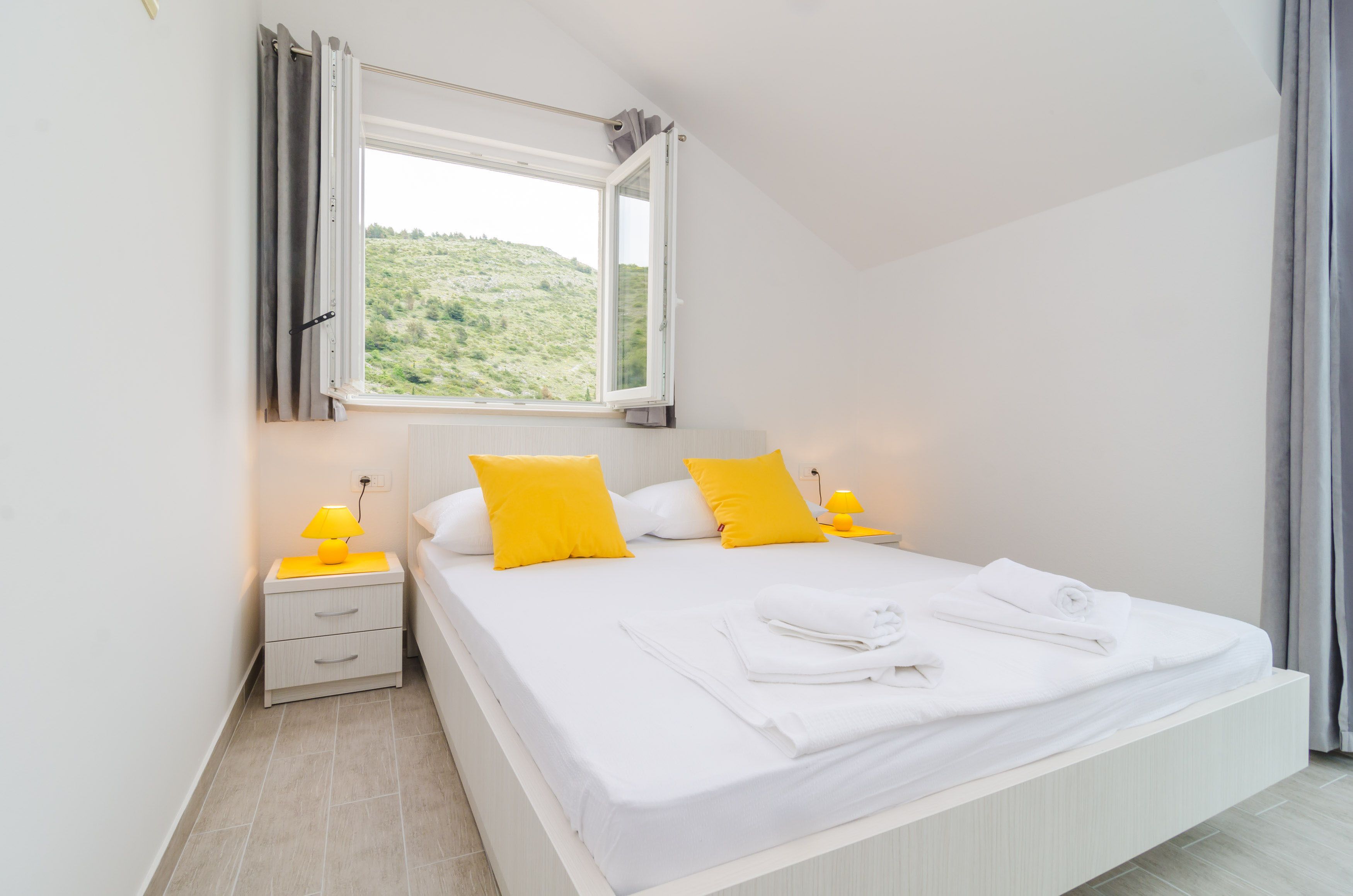 A bedroom with a bed, two bedside lamps, a nightstand, and a window with curtains.