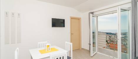 A modern apartment with a balcony, a dining area, and a TV on the wall.