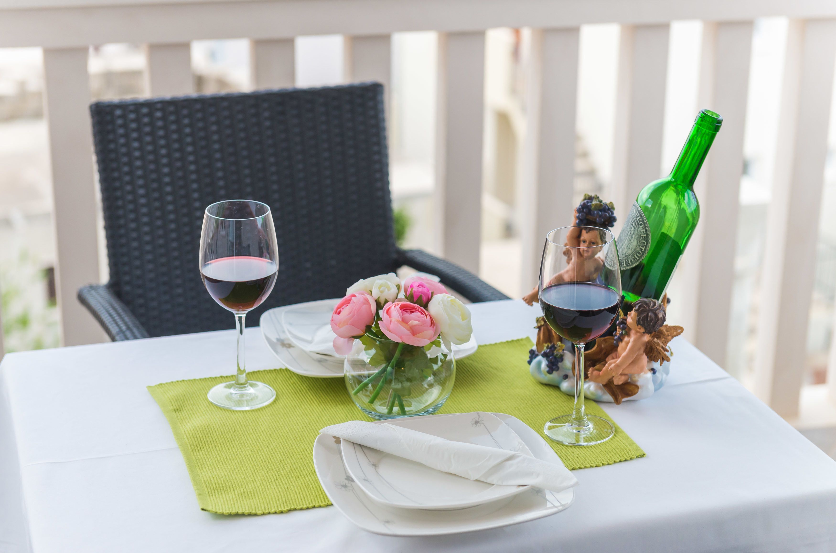 Une table dressée avec un verre à vin, un vase de fleurs et une bouteille verte.