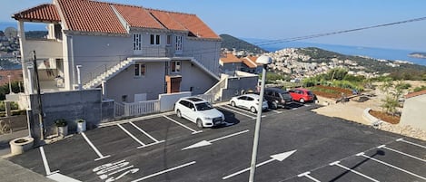 Ein Parkplatz mit Autos, ein Gebäude mit rotem Dachturm und Blick auf eine Küstenstadt.
