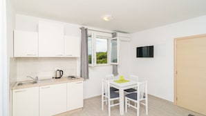 A compact kitchen with white cabinets, a sink, and a window with curtains. - Apartments Villa Dadic (Dubrovnik)