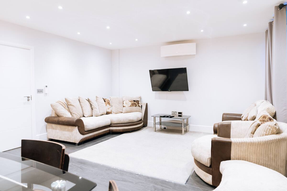 A modern living room with a sectional sofa, a round armchair, a flat-screen TV mounted on the wall, and a glass coffee table.