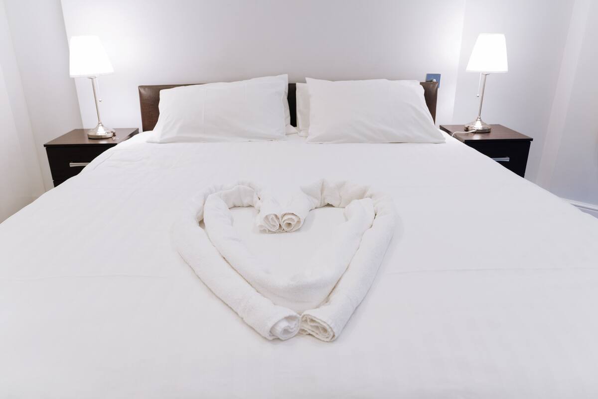 A neatly made bed with white linens and a heart-shaped towel arrangement in the center.